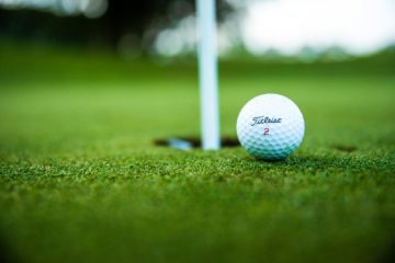 A close-up shot of a Titleist golf ball close to the hole on a green golf course.